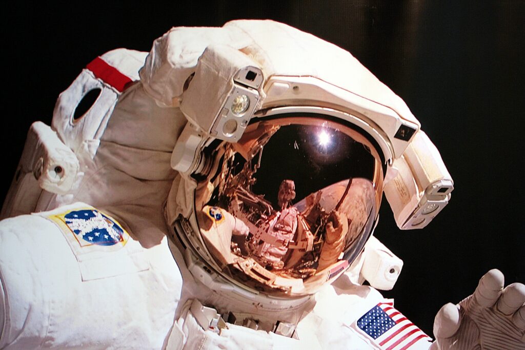 An astronaut's reflection visible in another astronaut's helmet visor during a spacewalk